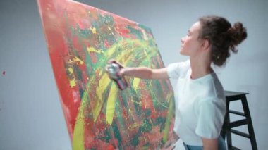 Modern sanat, genç kadın ressam beyaz bir odada büyük bir tuvale sprey boyayla resim çizer, yetenekli bir sanatçı ise soyutlama bir renk çizer..