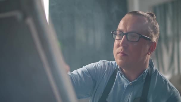 Persona creativa al lavoro, un artista maschio adulto di talento disegna un quadro astratto su una grande tela, artista in camicia blu e occhiali, 4k rallentatore. — Video Stock