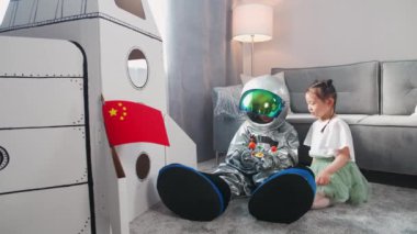 Asyalı çocuklar evdeki oturma odasında oynuyorlar, astronot kostümlü bir çocuk kız kardeşiyle yerde oturuyor, çocuklar güneş sisteminin oyuncak modeliyle oynuyorlar, 4k yavaş çekim..