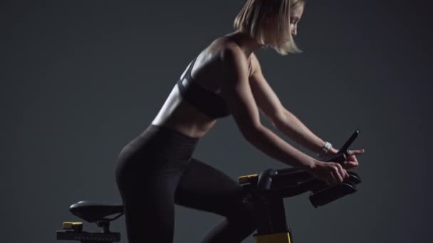 Ung kvinna är engagerad i en modern spinncykel, utför aerob uthållighetsträning på simulatorn i gymmet. — Stockvideo