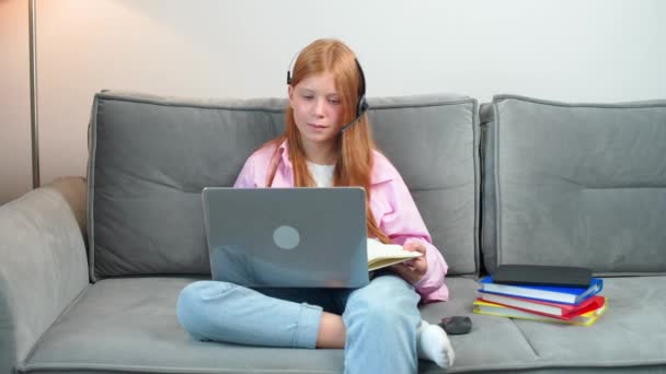 Uzaktan öğrenme, oturma odasındaki kanepede oturan kızıl saçlı genç kız ve evde tek başına ders çalışmak için dizüstü bilgisayar kullanıyor, videoyla evde eğitim görüyor, salgın sırasında ders çalışıyor. — Stok video