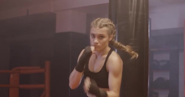 Mujer combate entrena sus golpes, día de entrenamiento en el gimnasio de boxeo, la chica entrena una serie de golpes y mira a la cámara. — Vídeos de Stock