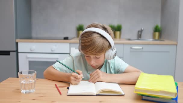 Distance learning, caucasian teen boy sitting at workplace in living room and uses a laptop to study in self-isolation at home, homeschooling online by videocall, the boy writes in a notebook. — Stock Video