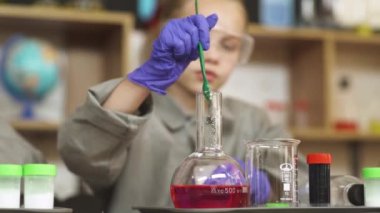 Bir kimya dersinde laboratuvar tecrübesi, bir kız elinde kırmızı bir sıvıyla cam bir şişe tutuyor ve içeriğini karıştırıyor, okulda modern eğitim..