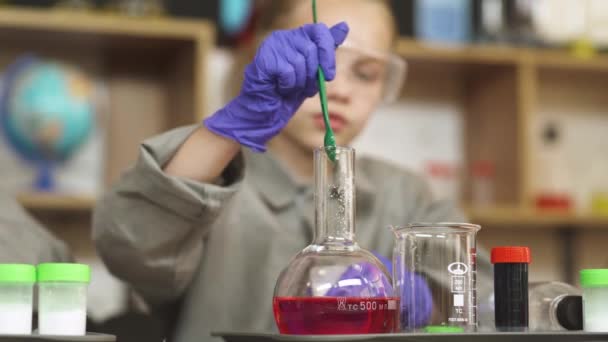 Experiencia de laboratorio en una lección de química, una niña sostiene una botella de vidrio con un líquido rojo y mezcla su contenido, la educación moderna en la escuela. — Vídeo de stock