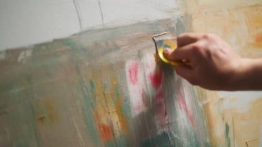 Soyut bir resim yapan yetenekli bir sanatçı, tuvali yağlı boya ile kaplıyor, arka planı hazırlıyor ve çiziyor, ellerin yakın plan görüntüsü, 4k yavaş çekim.
