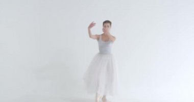 Beyaz etekli zarif bir kadın, bale yapıyor ve beyaz arka planda koreografik elementler sergiliyor..