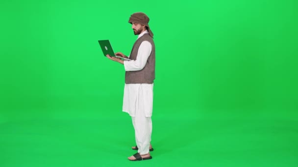Frilansare, man av arabiskt utseende i traditionella kläder använder en bärbar dator för att surfa på internet medan står mot bakgrund av en chromakey. — Stockvideo