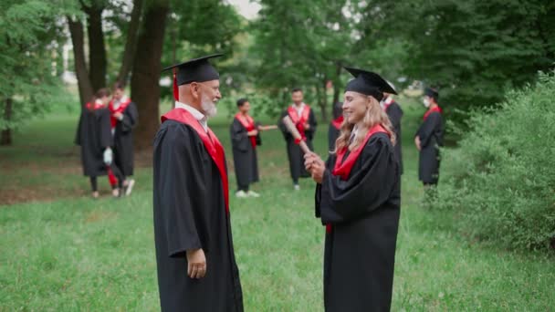 Міжнародний випускник університету, старший викладач вітає випускницю з отриманням диплому, жінка в одязі випускників тримає в руках диплом, емоційний момент, 4k повільний — стокове відео