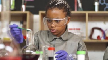Kimya dersinde laboratuvar tecrübesi, Afrikalı bir kız ayırıcıları cam bir şişede karıştırıyor, okulda modern eğitim....