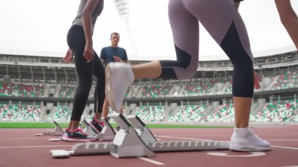 Movimento lento, jovens velocistas estão treinando no estádio, duas mulheres esportivas estão competindo em corrida de curta distância, o homem treinador controla o tempo. — Vídeo de Stock