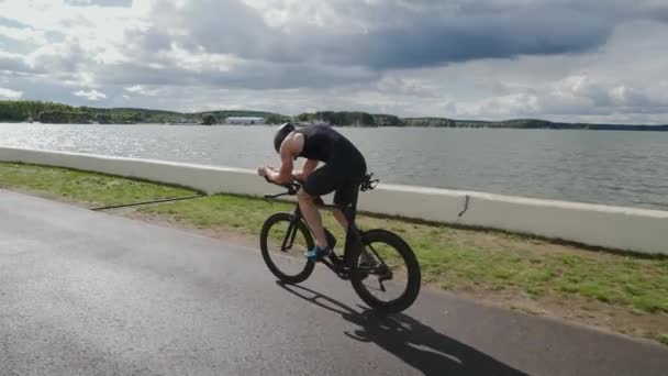 Triatleta monta uma bicicleta de corte, passeios de ciclista profissional em uma pista perto de um lago, treinamento de atleta para corrida, 4k super câmera lenta. — Vídeo de Stock