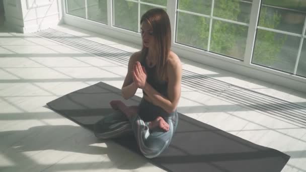 Joven hembra medita y hace yoga, un estado de ánimo tranquilo, relajándose en una habitación blanca llena de luz, la chica está sentada en el suelo. — Vídeos de Stock