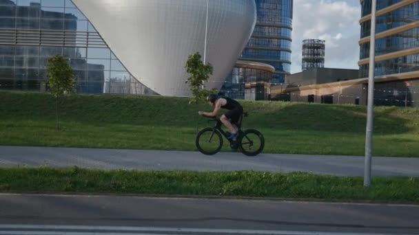 Um triatleta resistente monta uma bicicleta, passeios de ciclista profissional em uma estrada da cidade, trens de atleta em um ambiente urbano em uma bicicleta de corte, 4k câmera lenta. — Vídeo de Stock
