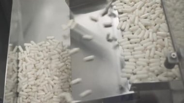 İlaç ve uyuşturucu üretimi, hareket halindeki beyaz kapsüller, taşıyıcıdaki tabletler, otomatikleştirilmiş üretim hattı.