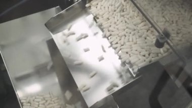 İlaç ve ilaç üretimi, çok sayıda hareket halindeki kapsül, taşıyıcıda beyaz tabletler, üretim hattında ilaçlar.