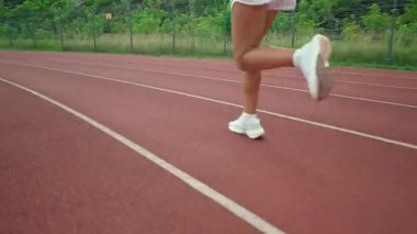 Sabah koşusu, sportif bir kadın güneşli bir günde stadyumda koşar. Düşük açılı bacak manzarası, profesyonel koşucu maratonu günlük antrenman..