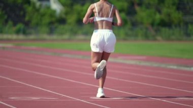 Sabah koşusu motivasyonu, sportif bir kadın güneşli bir günde stadyum pistinde koşuyor, arka görüş, profesyonel koşucu maratonu günlük antrenmanı, ileri doğru gidiyor..