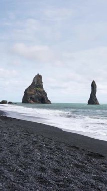 Dikey video, İzlanda manzarası, okyanus manzarası ve ufuktaki görkemli uçurumlar, devasa kıyı bölgesi, toprak dokusu, koyu kum, kıyı doğası arka planı, el bilgisayarı..