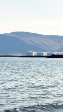 Yavaş çekim, deniz manzarası, büyük beyaz tanklar, petrol ve yakıt depolama tesisleri, ufuktaki dağlar, endüstriyel İzlanda manzarası..