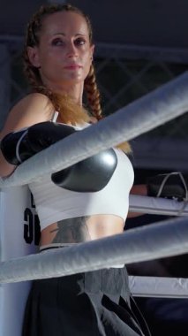 Süper yavaş çekim, bir kadın dövüşçünün dikey portresi ringin kenarında duruyor, bekliyor, sıkı eğitime hazırlanıyor, kadın gücü.