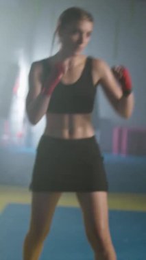 Ağır çekimde, profesyonel kadın boksör kum torbasına vuruyor ve tekmeliyor, yumruklarını eğitiyor, boks salonunda sıkı antrenman yapıyor, kadın hızlı vuruyor..