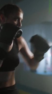 Kadın boksör kum torbasını dövüyor, yumruklarını eğitiyor, boks salonunda sıkı antrenman yapıyor, kadın hızlı, dikey video çekiyor..