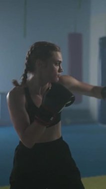 Profesyonel kadın boksör, boks salonundaki antrenman gününde yumruklarını çırpıyor ve eğitiyor. Kadın hızlı, dikey video çekiyor..