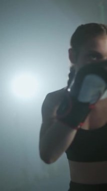 Profesyonel bir kadın boksör kum torbasını döver yumruklarını, kadın gücünü, kadın hızlı, yavaş çekimde dikey videoya saldırır..