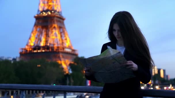 Mädchen auf der Suche nach einem Platz auf der Karte in Paris am Eiffelturm am Abend — Stockvideo