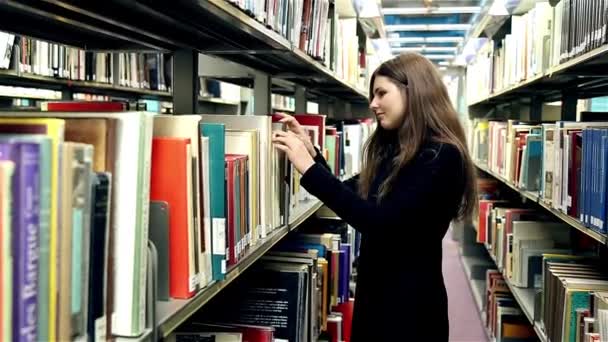 Девушка ищет книгу в библиотеке — стоковое видео