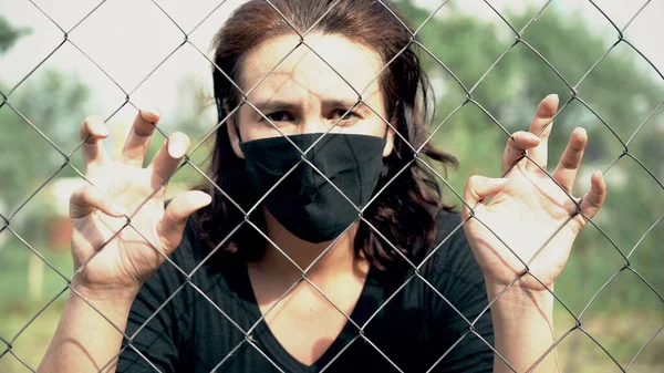 Mujer en máscara médica en shock deprimido a través de la cerca de alambre birbed, en concepto de aislamiento, corona Fotos De Stock