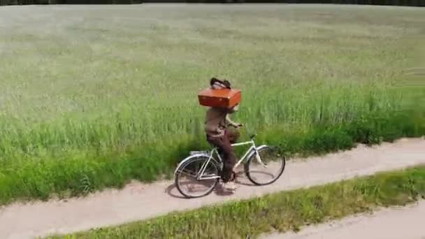 Muž sám kráčí po venkovské silnici v zeleném poli, drží kufr v ruce, legrační cestovní koncept — Stock video