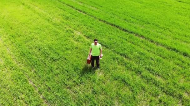 Сумний спантеличений чоловік один стоїть в зеленому полі, тримаючи валізу в руці, повітряний постріл з дрону — стокове відео