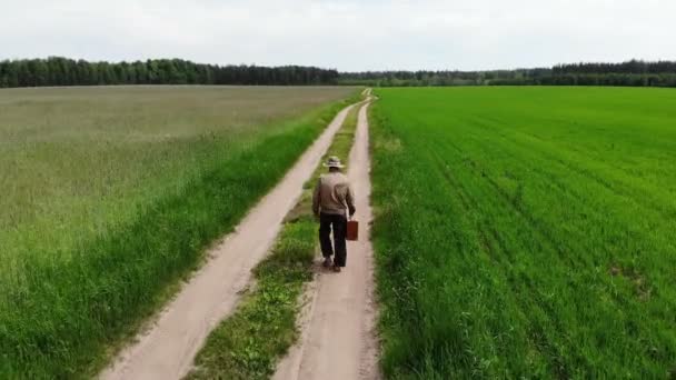 Hombre solo perdido y decepcionado caminando solo en la desesperación con la maleta por el camino del campo en un verde — Vídeo de stock
