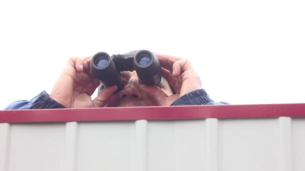 Mann mit Fernglas springt über Zaun und schaut sich um — Stockvideo