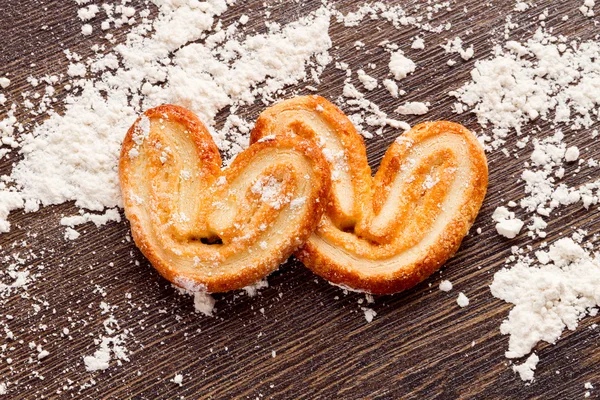 Cooking sweet cookies in shape of heart on wooden table with flo