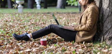 Dizüstü bilgisayar ile parkta oturan genç güzel kadın