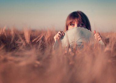 Genç, güzel bir kız, buğday tarlasında. Kız, geniş kenarlı mavi bir şapkanın arkasından dışarı bakar..