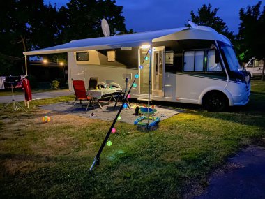 Fotoğrafta bir karavan ve kampçı akşamları kamp yerindeymiş.