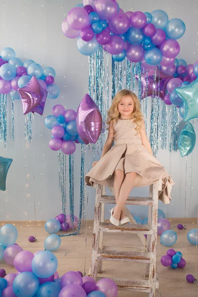 Szép kislány ül egy lépcsőn egy stúdióban, sok-sok színes léggömbök — Stock Fotó