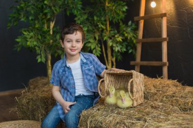 Sevimli çocuk saman üzerinde kuşlar ile sepet yanında oturan