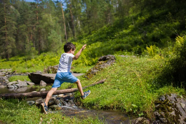Мальчик перепрыгивает через ручей в лесу — стоковое фото