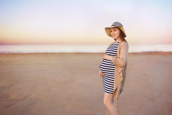 Uma jovem grávida está em uma praia e coloca as mãos em uma barriga — Fotografia de Stock