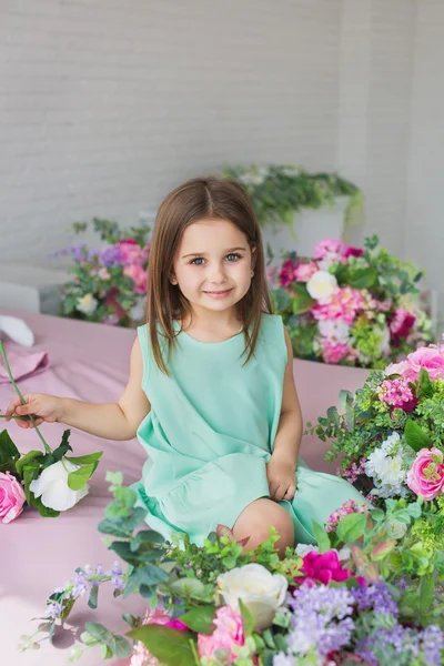 Szép kislány egy türkizkék ruhában közelében, egy virágot, egy stúdióban portré — Stock Fotó