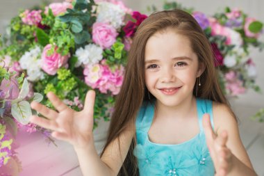 Eller bir çiçek yakın turkuaz elbiseli bir gülümseyen güzel küçük kız portresi tutar