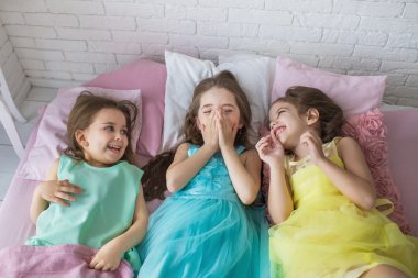 Üstten Görünüm: Üç küçük kız bir yatak ve gülümseme yalan