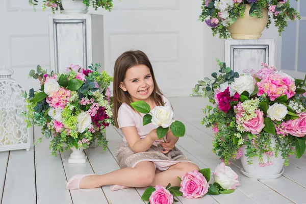 Szép kislány, egy könnyű rózsaszín ruhát a padlón ül, és tart egy virág, egy stúdióban — Stock Fotó