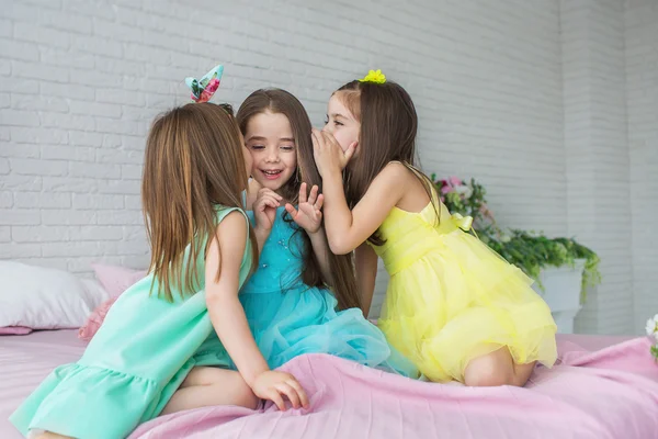 Tři krásná malá Děvčata sedí na posteli a šeptat vzájemně — Stock fotografie