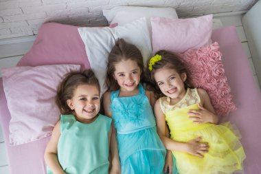 Üstten Görünüm: Üç küçük kız bir yatak ve gülümseme renkli elbiseler yalan